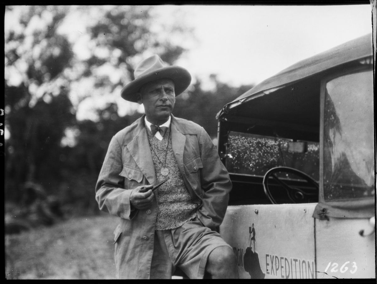 Photograph of Hans Hermann Schomburgk standing beside an expedition vehicle bearing the Schomburgk Expedition emblem.